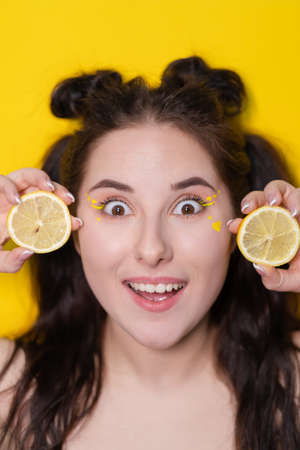 brunette woman girl with lemon near skin face on yellow background. tasty juicy fruit. Tropical fruits, Healthy food. citrus slice.の写真素材