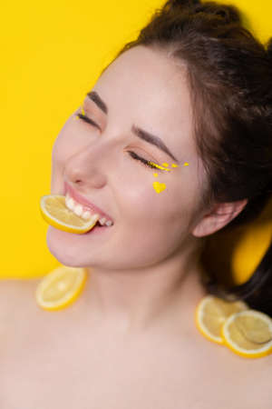 brunette woman girl with lemon near skin face on yellow background. tasty juicy fruit. Tropical fruits, Healthy food. citrus slice.の写真素材