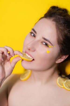 young woman with lemon slices, brunette girl with bare shoulders holding lemon near face on yellow background. citrus fruits, Healthy food. tasty juicy fruitの写真素材