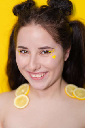 young woman with lemon slices, brunette girl with bare shoulders holding lemon near face on yellow background. citrus fruits, Healthy food. tasty juicy fruitの写真素材