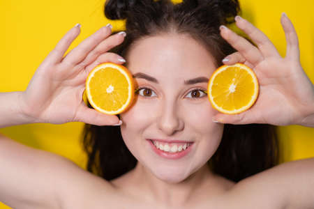 young brunette woman girl with slice of orange fruit near skin face on yellow background. tasty juicy fruit. Tropical fruits, Healthy food. citrus slice. tasty juicy fruit.の写真素材