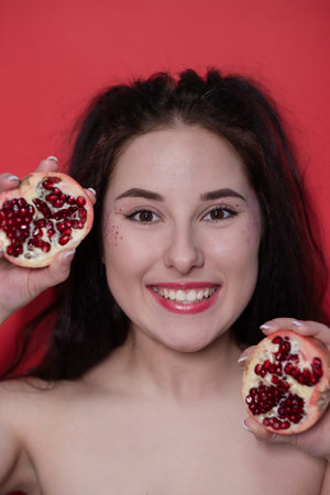 charming brunette woman girl female with cropped half pomegranate near skin face on red background. tasty juicy fruit.の写真素材
