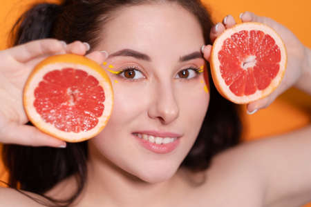sweet joyful brunette woman girl female with cropped slice of grapefruit near skin face on orange background. tasty juicy fruit. Tropical citrus fruits, Healthy food. weight loss.の写真素材