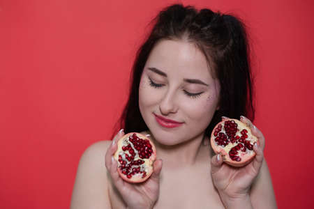 portrait brunette woman girl female with pomegranate near face on red background. tasty juicy fruit.の写真素材