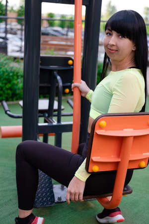 sporty woman in black and green sportswear doing sport exercises outside on sport playground....