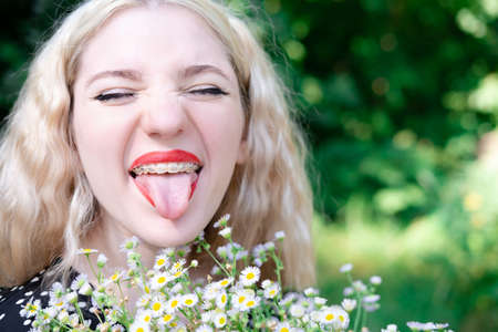 portrait of a charming blonde teenage girl wearing teeth braces with bouquet of white wildflowers....