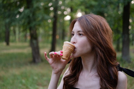 Smiling cheerful ukrainian brunette young woman eating ice cream outdoors.の写真素材