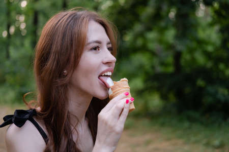 Smiling cheerful ukrainian brunette young woman eating ice cream outdoors.の写真素材