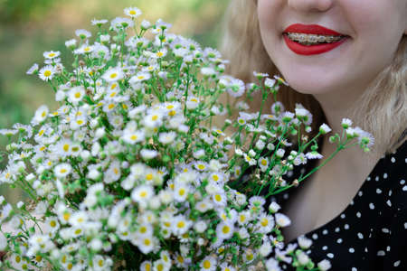 portrait of a charming blonde teenage girl wearing teeth braces with bouquet of white wildflowers. female with braces in mouth. healthy teeth. orthodontist dentist.の写真素材