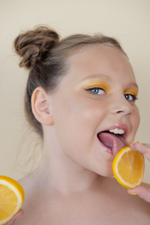 sweet cute girl school age holding a ripe fresh lemon on yellow background. child with fruit on colorful background. summer citrus food.の写真素材