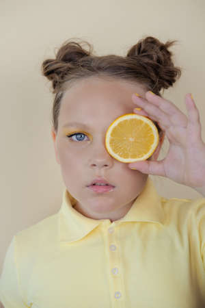 sweet cute girl school age holding a ripe fresh lemon on yellow background. child with fruit on colorful background. summer citrus food.の写真素材