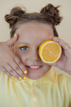 sweet cute girl school age holding a ripe fresh lemon on yellow background. child with fruit on colorful background. summer citrus food.の写真素材