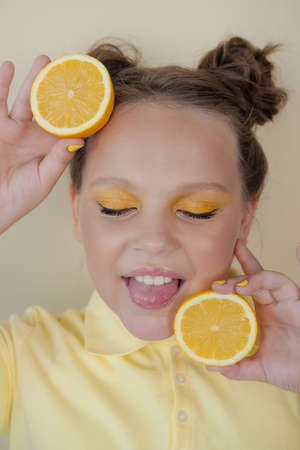 sweet cute girl school age holding a ripe fresh lemon on yellow background. child with fruit on colorful background. summer citrus food.の写真素材
