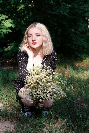 touching portrait of a charming blonde girl with bouquet of white wildflowers. female with flowers.の写真素材