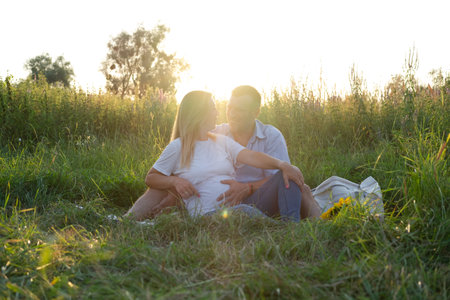 Outdoor family portrait: beautiful young pregnant female and her husband, hands on belly, anticipate child, enjoy togetherness. Happy future parents expecting a baby soon.の写真素材
