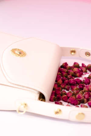 fashion photo of purse. white woman handbag near little roses flowers. isolated on white and pink background. product composition photography.の写真素材