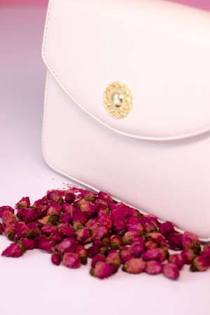fashion photo of purse. white woman handbag near little roses flowers. isolated on white and pink background. product composition photography.の写真素材