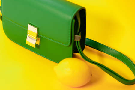stylish little green purse or handbag on yellow background with a lemon nearby. product composition photography. bag and reticule for women.の写真素材