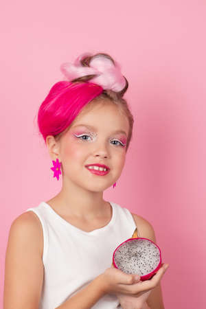 sweet Girl is holding a Pitahaya near her face. A pitaya fruit hold in hand on pink background. Tropical Dragon Fruit cut in half. space for textの写真素材