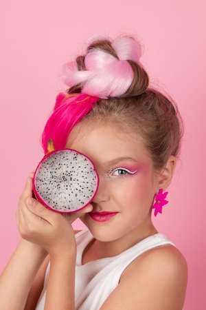 sweet Girl is holding a Pitahaya near her face. A pitaya fruit hold in hand on pink background. Tropical Dragon Fruit cut in half. space for textの写真素材