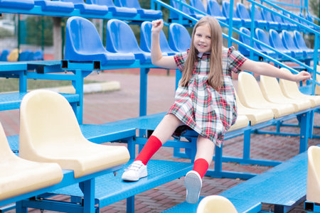 pretty girl in school dress uniform on the blue and yellow tribune of the school stadium. school time. tweenの写真素材