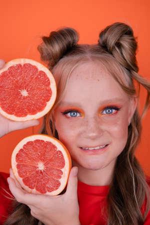 pretty tween girl in orange with a grapefruit isolated on orange background. tropical citrus fruits Grapefruit slices. orange stylish make up. teenager portrait.の写真素材