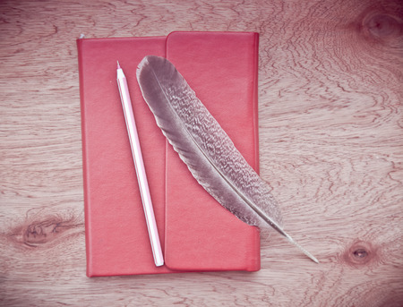 red notebook with  Feather and pen  on wooden table,vintage filterの写真素材