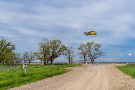 Russian biplane AN-2 flies over the field and road