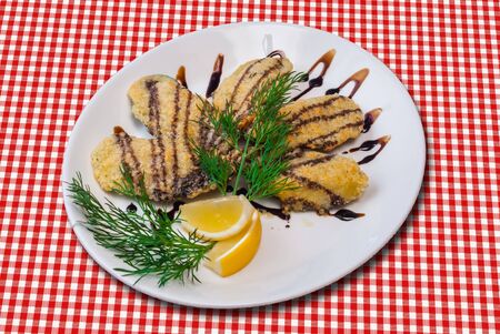 Fried fish fillet served wirh sauce, lemon and dill on checked tablecloth