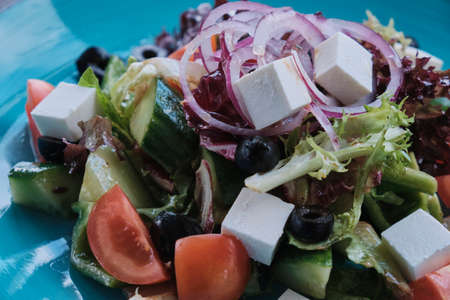 Greek salad on wooden table decorated with spices, daylight shot