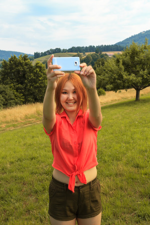 Asian smiling young woman does selfi in picturesque countryside in summerの写真素材