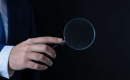 businessman in black background in the hands of a magnifierの写真素材