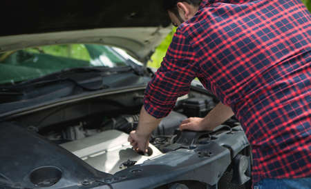 A man fixes a broken car on a city street.
