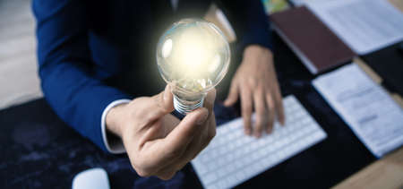 businessman in the office holds a shining lamp, the symbol of the idea; business conceptの写真素材