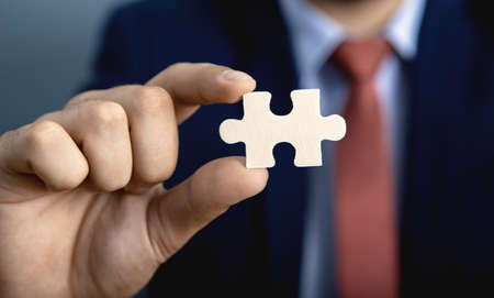 Businessman standing on gray background holds a piece of the puzzle in his handの写真素材