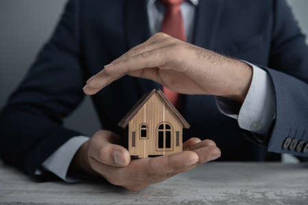 insurance; businessman holds a wooden house in his handsの写真素材