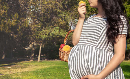 pregnant woman eats fruit while walking in the gardenの写真素材