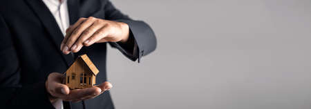 businessman on a gray background holds a house in his hand; business conceptの写真素材