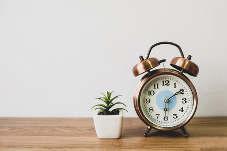 The clock is placed on the table with a tree pot placed on the side with a white background.の写真素材