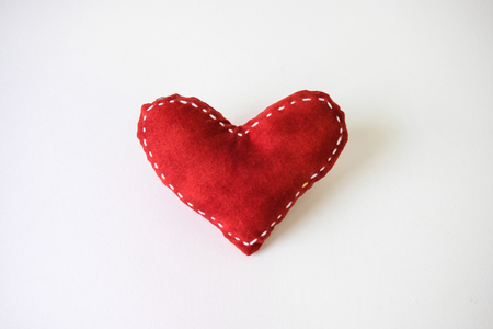 Red heart made of cloth placed on a white table.の写真素材