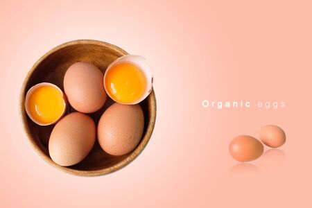 Organic eggs placed in a wooden bowl with a pink backgroundの写真素材