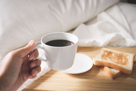 Coffee bread in a white cup placed on the bed, white linen during the morning, fresh airの写真素材