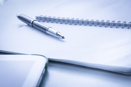 Open notebook with metallic ball pen and tablet. Selective focus and blue effect.の写真素材