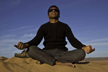 attractive young african man meditating in the desertの写真素材