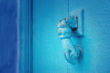 Iron door handle in the shape of a hand at a blue wooden, moroccan door in Chefchaouen.