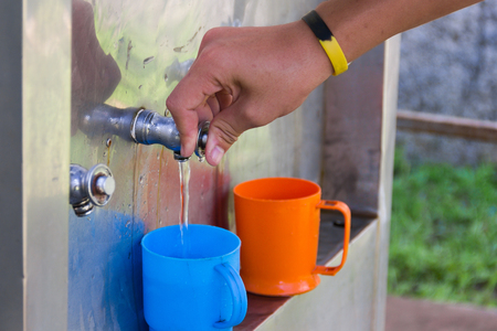 Male students use hand pressed water from a water-cooler into blue plastic glass to drink.の写真素材