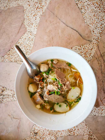Clear Soup Pork Noodle in a white cup placed on a stone floor.