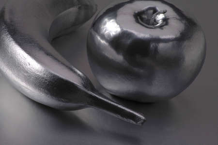 A chrome banana and apple on a silver background.の写真素材