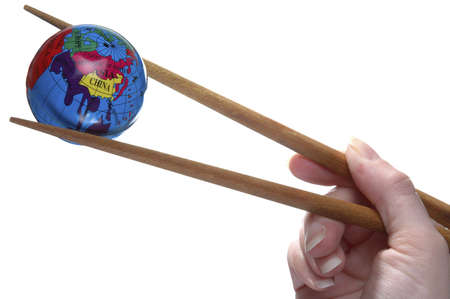 A miniature globe held in a pair of chopsticks.の写真素材
