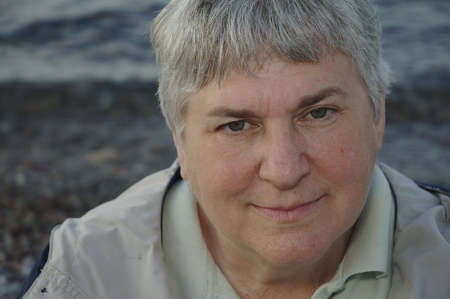 A portrait of a gray-haired woman with the lakeshore as a background.